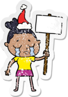 hand drawn distressed sticker cartoon of a crying woman with protest sign wearing santa hat png