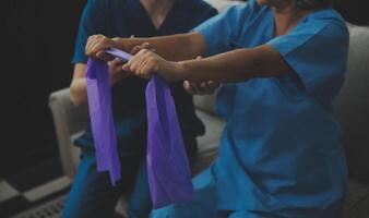 Personal trainer assisting senior woman with resistance band. Rehabilitation physiotherapy worker helping old patient at nursing home. Old woman with stretch band being coached by physiotherapist. photo