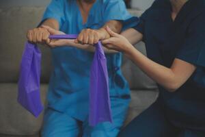 Personal trainer assisting senior woman with resistance band. Rehabilitation physiotherapy worker helping old patient at nursing home. Old woman with stretch band being coached by physiotherapist. photo