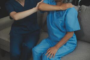 Old woman training with physiotherapist using dumbbells at home. Therapist assisting senior woman with exercises in nursing home. Elderly patient using dumbbells with outstretched arms. photo