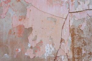 Gray concrete wall with cracks and scratches covered with shabby pink plaster photo