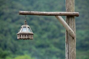 Thai traditionan wooden lantern hang on wooden post with green blurred background. photo