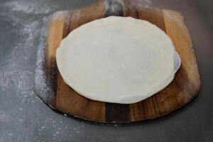 Fresh raw pizza dough on wooden tray photo