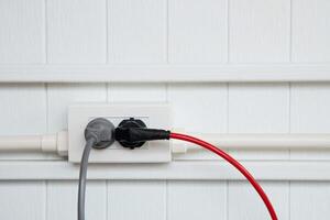 An electric plug with a gray and red cable in the socket. photo