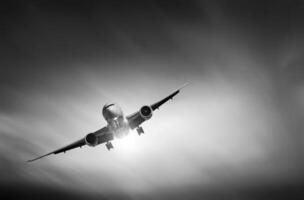 A commercial passenger plane flying above the clouds in the black and white sky. The concept of fast travel, vacation and business. Plane against sky photo