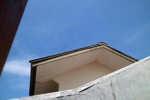 view of a house roof and walls with a view of the bright blue sky photo