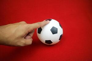 a hand holding a small white and black toy rubber ball. Red background photo