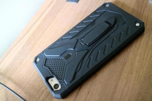 a smart phone with a black hard case with a robot style. placed on a wooden table photo