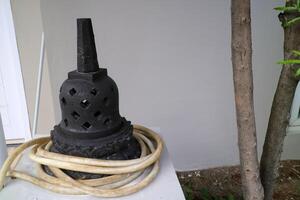 an artificial stupa made of cement. For outdoor decoration. black, with a water hose wrapped around it photo