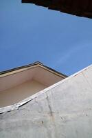 view of a house roof and walls with a view of the bright blue sky photo