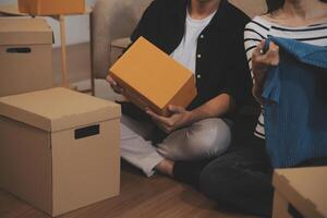 Two Asian blogger showing clothes in front of the camera to recording vlog live streaming at her shop. Online Shopping Cart notion. on sofa at home photo