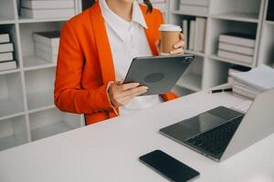 atractivo sonriente joven asiático negocio mujer trabajo a hogar oficina, asiático mujer trabajando en ordenador portátil computadora participación tableta. foto