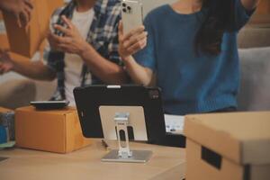 Two Asian blogger showing clothes in front of the camera to recording vlog live streaming at her shop. Online Shopping Cart notion. on sofa at home photo