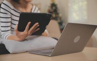 joven atractivo asiático mujer descansando utilizando hojeada tableta computadora en sofá a hogar, contento niña sentado en sofá relajarse leyendo digital artilugio con entusiasmado, comunicación y estilo de vida concepto. foto