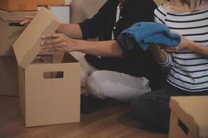 Two Asian blogger showing clothes in front of the camera to recording vlog live streaming at her shop. Online Shopping Cart notion. on sofa at home photo