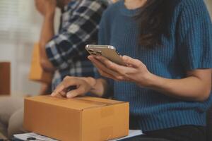 Two Asian blogger showing clothes in front of the camera to recording vlog live streaming at her shop. Online Shopping Cart notion. on sofa at home photo