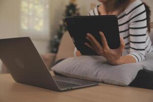 joven atractivo asiático mujer descansando utilizando hojeada tableta computadora en sofá a hogar, contento niña sentado en sofá relajarse leyendo digital artilugio con entusiasmado, comunicación y estilo de vida concepto. foto