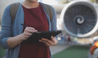 Blonde female tourist checking incoming notification on smartphone sitting on seat of airplane with netbook.Young businesswoman share media from telephone on laptop computer during plane flight photo