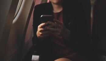 Blonde female tourist checking incoming notification on smartphone sitting on seat of airplane with netbook.Young businesswoman share media from telephone on laptop computer during plane flight photo