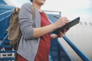 rubia hembra turista comprobación entrante notificación en teléfono inteligente sentado en asiento de avión con netbook.joven mujer de negocios compartir medios de comunicación desde teléfono en ordenador portátil computadora durante avión vuelo foto