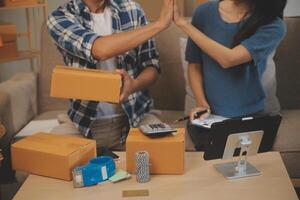 Two Asian blogger showing clothes in front of the camera to recording vlog live streaming at her shop. Online Shopping Cart notion. on sofa at home photo