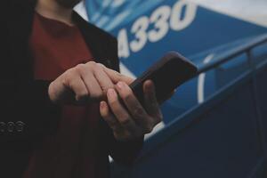 Young asian woman in international airport, using mobile smartphone and checking flight at the flight information board photo