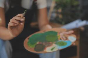 Cropped image of female artist standing in front of an easel and dipping brush into color palette photo