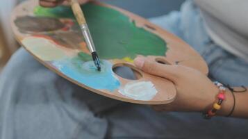 Cropped image of female artist standing in front of an easel and dipping brush into color palette photo