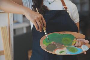 Cropped image of female artist standing in front of an easel and dipping brush into color palette photo