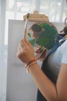 Cropped image of female artist standing in front of an easel and dipping brush into color palette photo