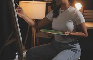 Cropped image of female artist standing in front of an easel and dipping brush into color palette photo