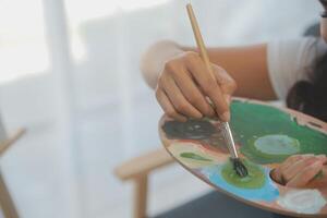 Cropped image of female artist standing in front of an easel and dipping brush into color palette photo