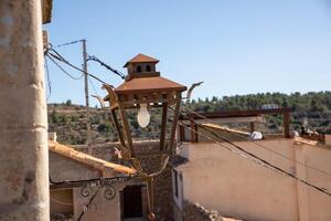 Old rusty iron lantern with a white light bulb on a stone wall against the blue sky over a small town photo