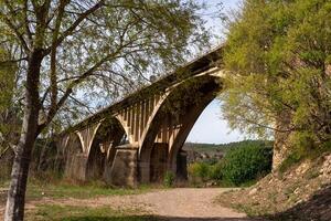 Stone and concrete arched road bridge over the river and hiking trail photo