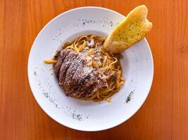 Italian fettuccine pasta with slice of beef steak and garlic bread on white plate. photo