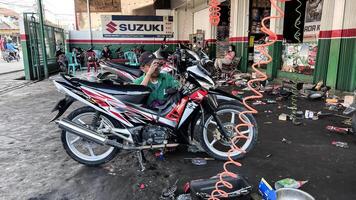 mecánico en mono haciendo diagnósticos de moto cerca caja de herramientas en taller. bekasi, Indonesia, abril 22, 2024 foto