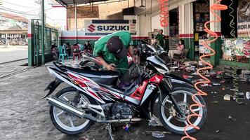 mecánico en mono haciendo diagnósticos de moto cerca caja de herramientas en taller. bekasi, Indonesia, abril 22, 2024 foto