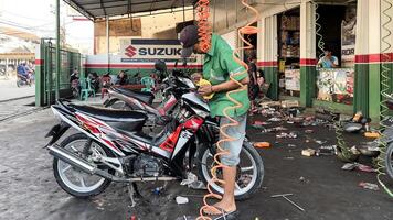 mecánico en mono haciendo diagnósticos de moto cerca caja de herramientas en taller. Jacarta, Indonesia, mayo 1, 2024 foto