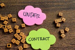 Concept of Under Contract write on sticky notes isolated on Wooden Table. photo