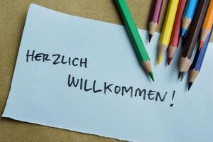 Concept of Herzlich Willkommen write on sticky notes isolated on Wooden Table. photo