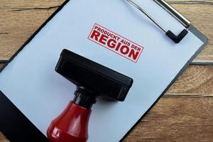 Red Handle Rubber Stamper and Produckt Aus Der Region in Language Germany text above paperwork isolated on wooden background photo