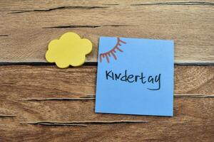 Concept of Kindertag in Language Germany write on sticky notes isolated on Wooden Table. photo