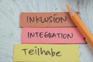 Concept of Inklusion, Integration, Teilhabe write on sticky notes isolated on Wooden Table. photo