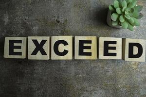 Concept of The wooden Cubes with the word Exceed on wooden background. photo