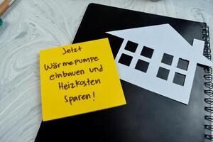 Concept of Jetzt Warmepumpe Einbauen und heizkosten sparen write on sticky notes isolated on Wooden Table. photo