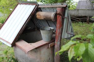 In rural areas, an ancient water well, featuring a concrete ring, iron cover, and a wooden lever for hoisting buckets, serves as a vital resource for agricultural water extraction on farms. photo