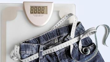 blue measuring tape is threaded into jeans instead of a belt, on a blue background, floor scales for weight control. copy space, concept of weight loss and weight control, measurement of body volume. photo