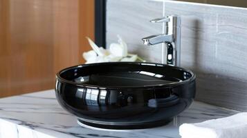 Stylish bathroom interior featuring a round black marble sink and a silver chrome faucet against a white wall. photo