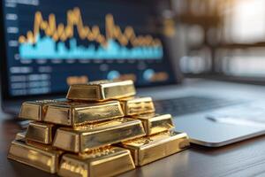 Gold bars are on the table next to a laptop showing a graph of financial growth. Concept of investment, wealth, stock exchange photo