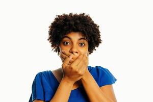 Surprised young african woman covering mouth with hands and staring at camera while standing over white background photo